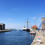 Campingplatz Zierow Blick auf eine lebendige Hafenpromenade mit Wasser, Schiffen und großem Riesenrad bei blauem Himmel an einem sonnigen Tag