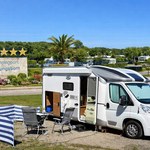 Weißes Wohnmobil mit aufgebautem Windschutz und Campingmöbeln auf dem 5-Sterne Campingpark Kühlungsborn bei sonnigem Wetter an der Ostsee