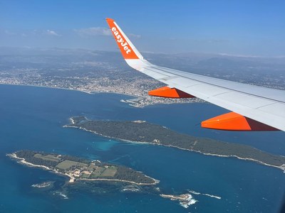 Flugangst- Zu sehen ist ein Flugzeugflügel am Himmel mit einer Insel darunter und das Meer