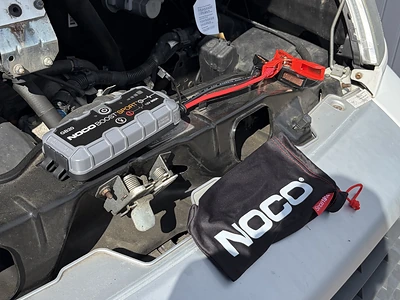 Zu sehen ist das NOCO Boost GB20: 500A UltraSafe Starthilfe Powerbank – 12V Lithium-Starthilfegerät & Starterkabel auf dem Motor liegend mit den beiden anschlusskabeln